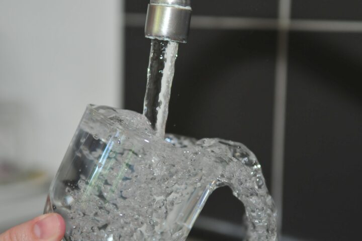 A hand holding a drinking glass under a running faucet.