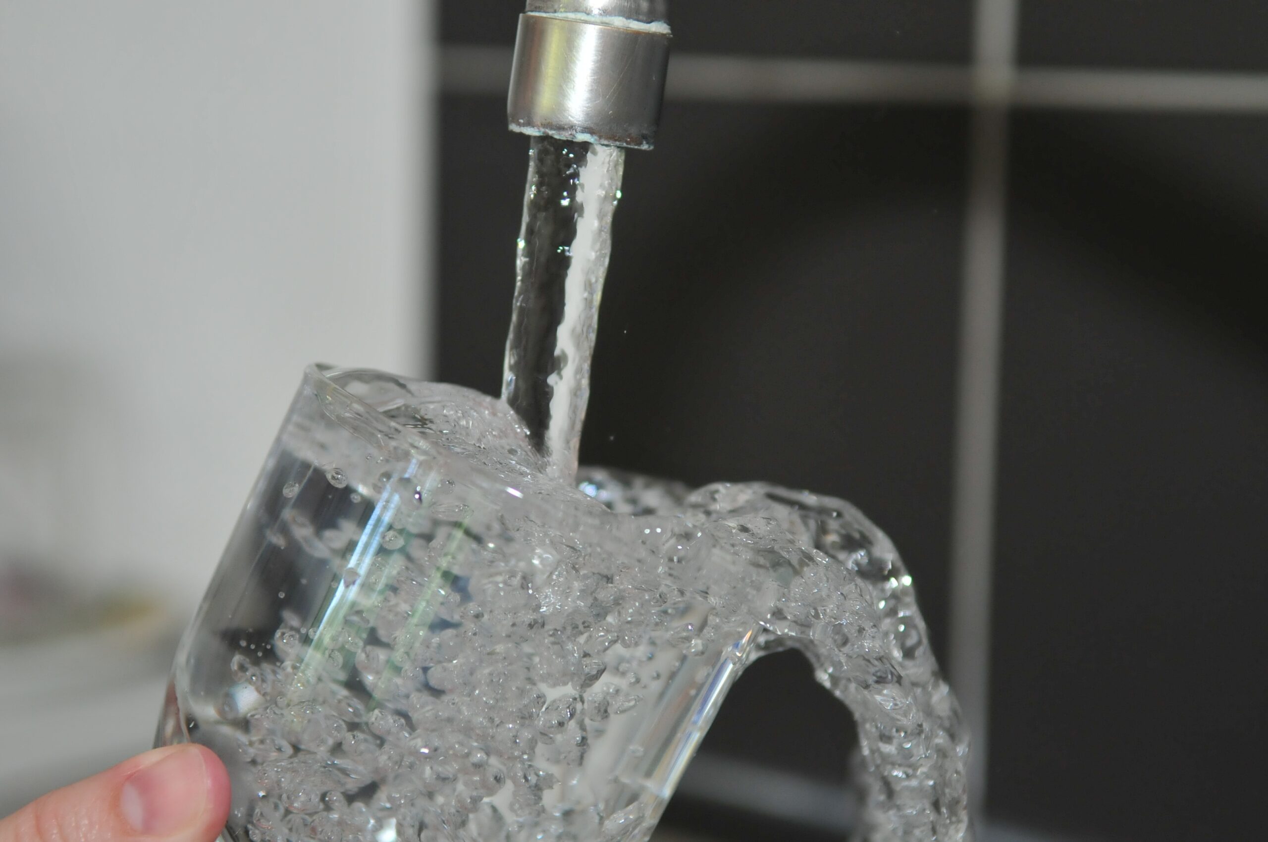 A hand holding a drinking glass under a running faucet.