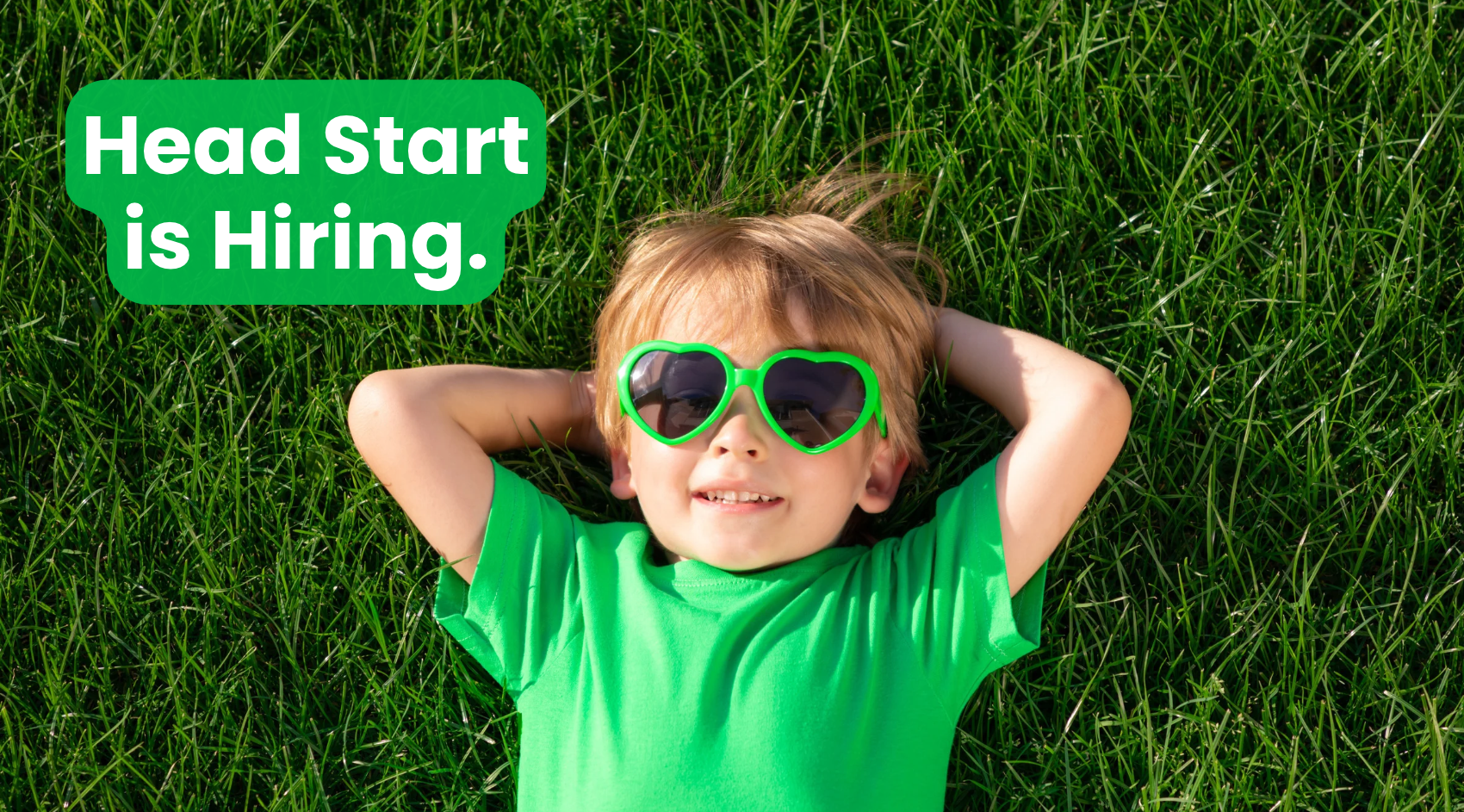 A young boy is lying on a patch of grass in a relaxed pose and wearing sunglasses. Text reads, "Head Start is Hiring."